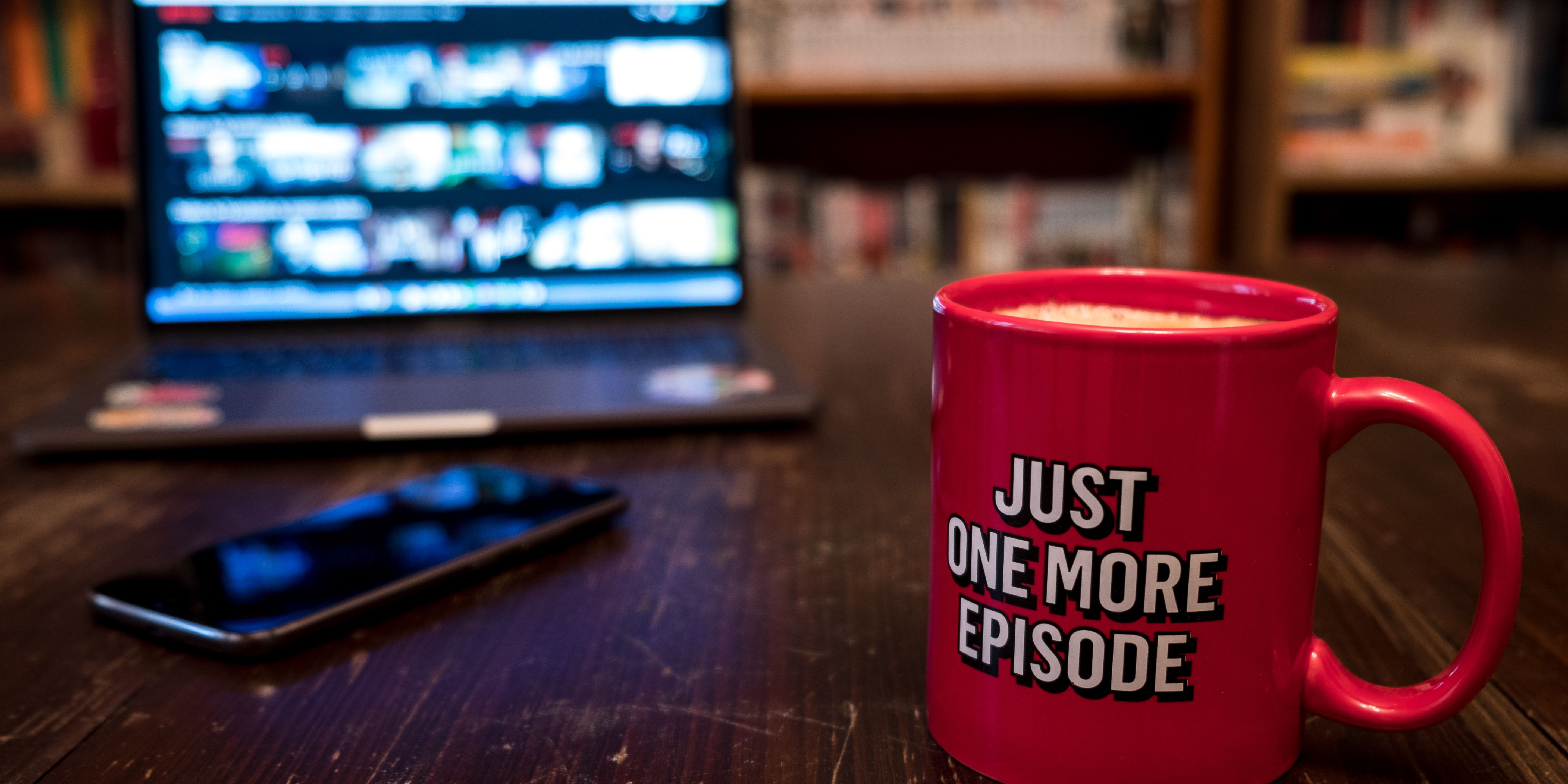 Watching series with a cup of tea on wood table with cellphone.